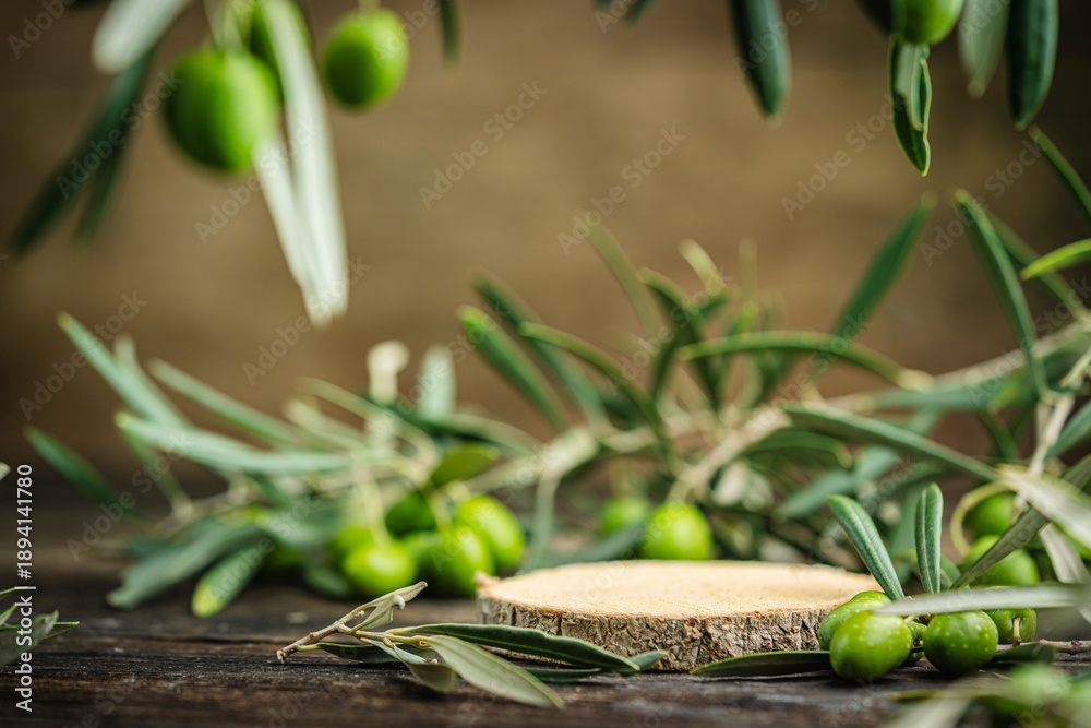 Fototapeta premium Olive branches with fresh green olives arranged on rustic wooden surface with a wooden slice in the center. Concept of Mediterranean agriculture, organic food, healthy lifestyle and natural background