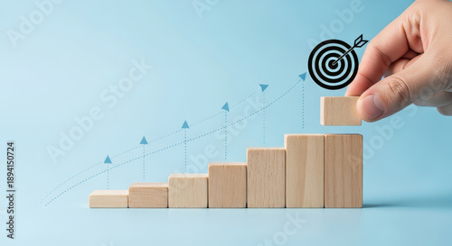 A hand places a wooden block, symbolizing progress and goal setting, against a light blue background featuring an upward trend and a target.