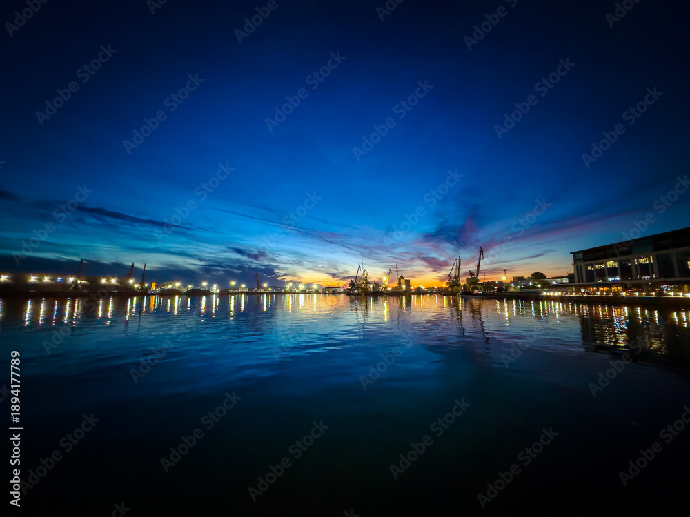 Obraz premium Sunset over the harbor with boats and cranes in the water reflecting colors