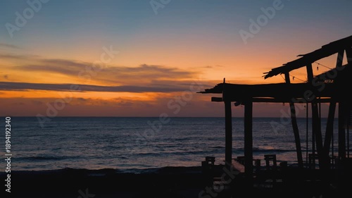Sunrise Over Ocean with Silhouetted Beach Bar Under Orange and Pink Sky