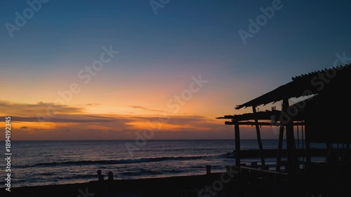 Sunrise Over Ocean with Silhouetted Beach Bar and Couple Walking Along Shore