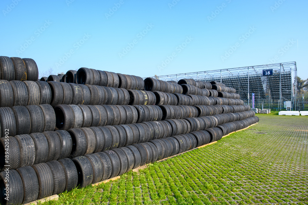 Fototapeta premium Stacked racing tires forming a safety barrier at Monza racetrack, Italy, under a clear blue sky, conveying speed, motorsport intensity, and track-side atmosphere.