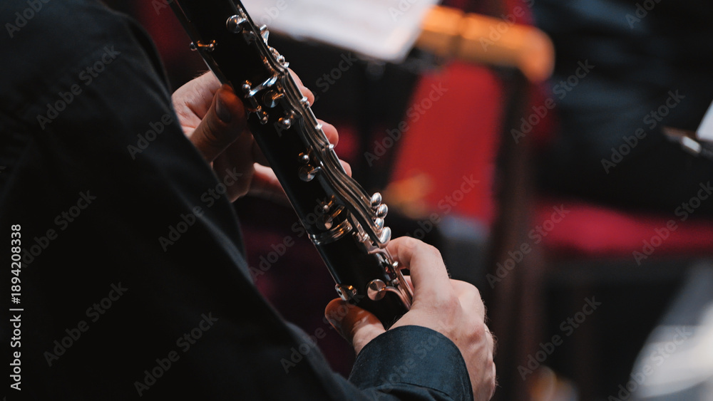 Obraz premium Close-up of a clarinetist's hands on the silver keys of a woodwind instrument during a classical performance. Focused lighting highlights the musician's skill in a concert hall setting