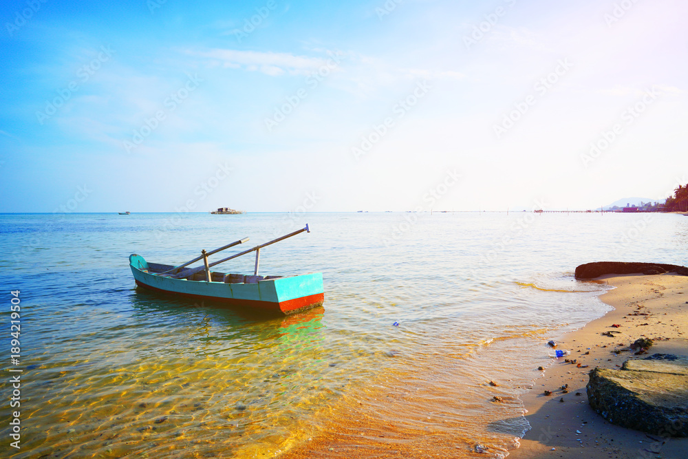 Naklejka premium Boat on shore at beach during late afternoon with clear sky and calm water in background. Small Fishing boat sits near shoreline on sea sandy beach. Ocean is clear and calm. Fishing wooden boat in sea