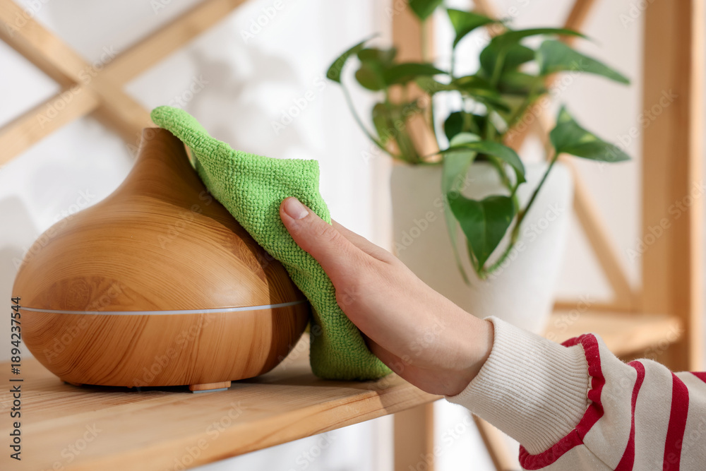 Fototapeta premium Woman wiping aroma lamp with microfiber cloth at home, closeup