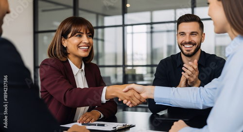 Group of corporate people happy with results of team work at meeting. Mature Latin bank worker woman shaking hand with client, recruit employee or business partner after signing collaboration contract