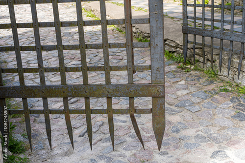 Vászonkép Rusty iron gate with sharp metal spikes on a stone courtyard, concept of security, restriction, protection and historical architecture