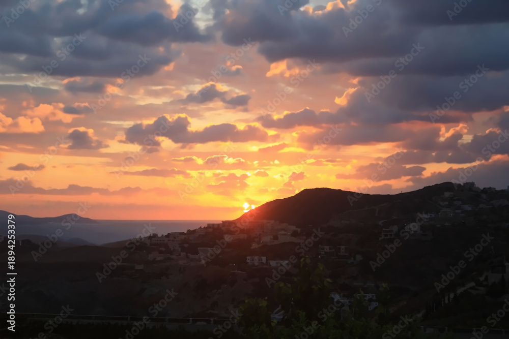 Obraz premium Dramatic Sunset Over Mediterranean Hillside Village with Golden Clouds
