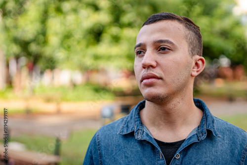 Serious young man in a blue denim shirt in a park