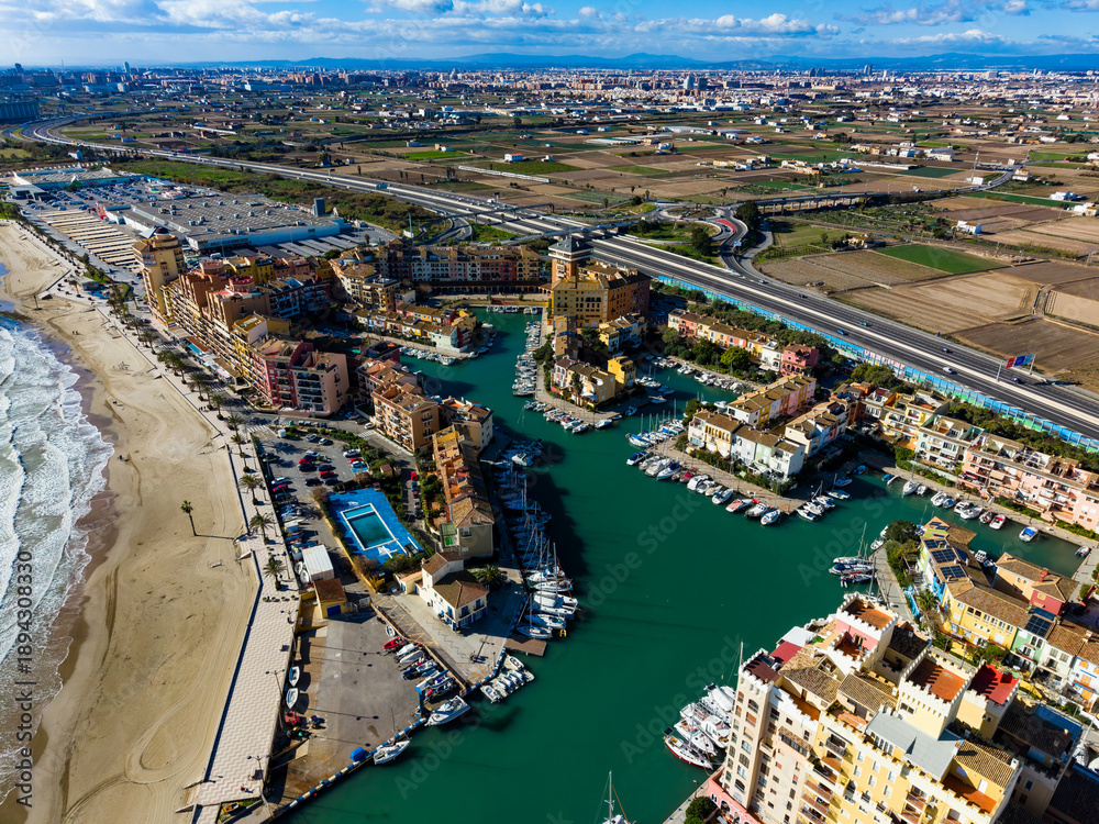 Obraz premium Coastal view of marina area with colorful buildings, water, and fields in background near city during daytime