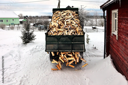 Photos Unloading split logs onto snow in front of rural house in winter time, firewood delivery truck brought logs to village with wood heating