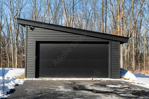 Modern black garage with slanted roof in winter forest setting