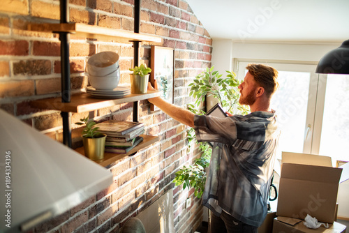Young man arranging shelves in sunny loft apartment