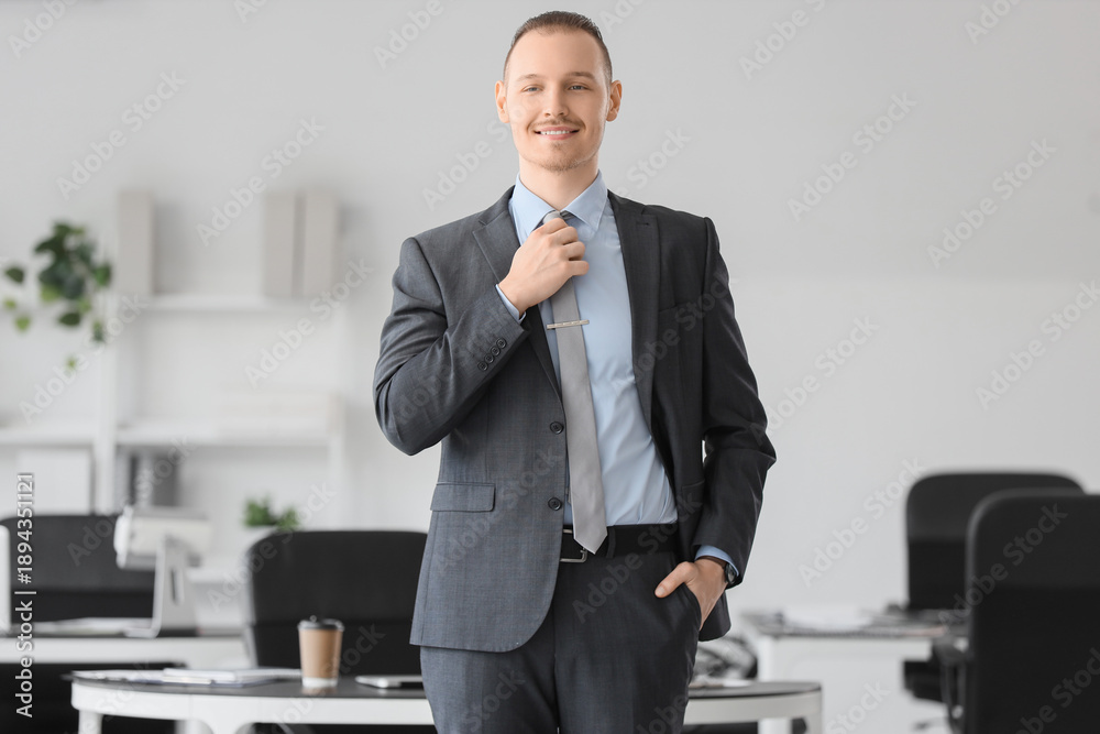 Fototapeta premium Portrait of handsome businessman fixing necktie in office
