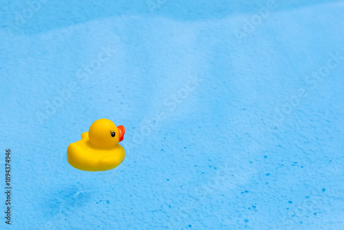 Horizontal close-up photo of a yellow rubber duck floating on the left side of a crystal clear blue swimming pool. Minimalist composition with ample copy space on the right for text