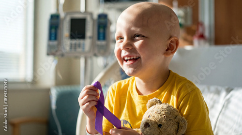 World Cancer Day-Caucasian child patient with bald head wearing yellow shirt showing bright smile holding purple ribbon and teddy bear in hospital room, joy hope support concept