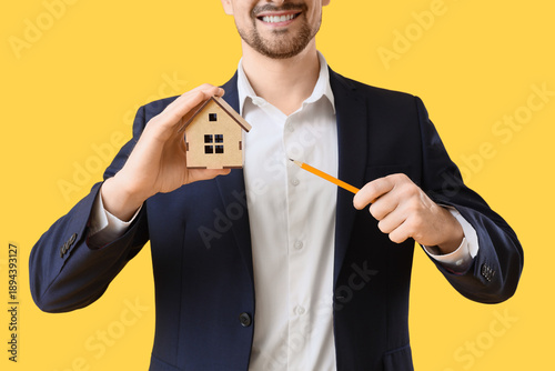 Male architect with house figure on yellow background, closeup