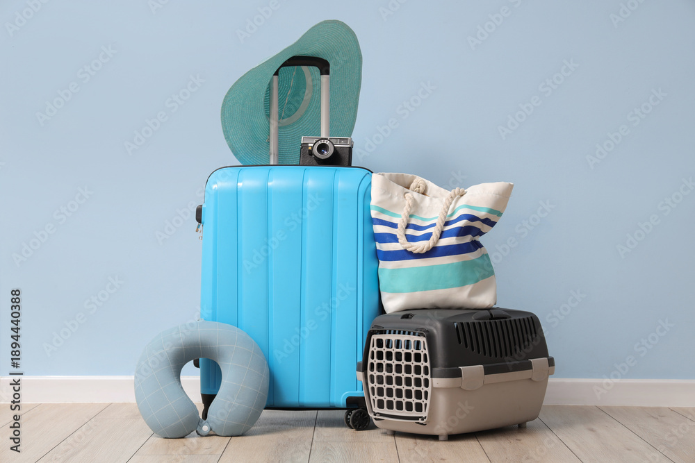 Fototapeta premium Packed suitcase with cat carrier, beach bag and camera near blue wall