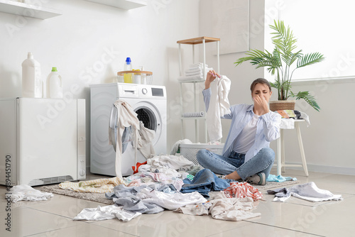 Fotografie Displeased young woman with smelly laundry near washing machine at home