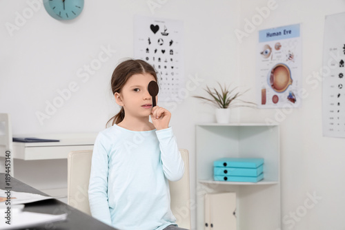 Cute little girl with occluder checking eyesight in clinic