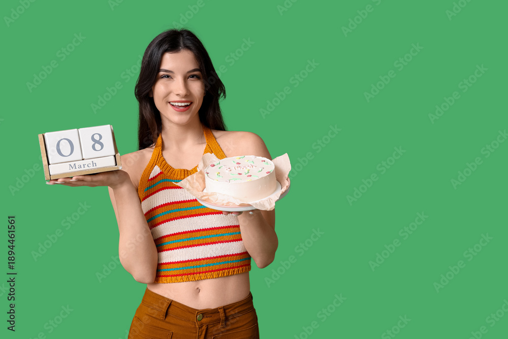 Fototapeta premium Beautiful young woman with sweet bento cake and cube calendar with date 8 MARCH on green background. International Women's Day