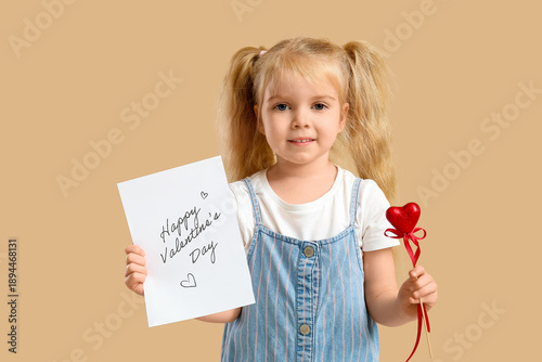 Cute little girl holding greeting card with text HAPPY VALENTINE'S DAY and heart on beige background