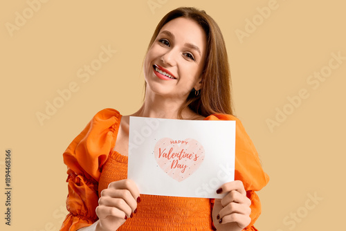 Beautiful young woman holding greeting card with text HAPPY VALENTINE'S DAY on beige background