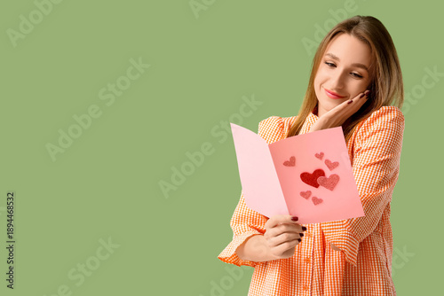 Happy young woman holding greeting card with hearts on green background. Valentine's Day celebration
