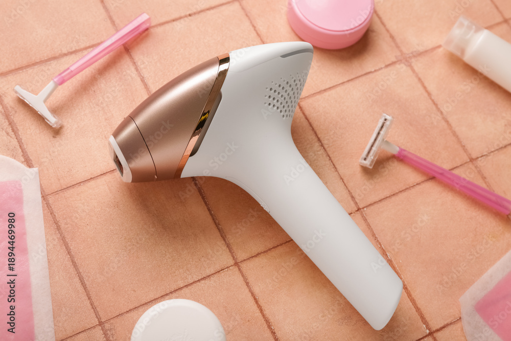 Fototapeta premium Modern photoepilator with wax strips, razors and cosmetic products on pink tile background