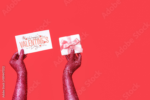 Painted female hands with greeting card and gift for Valentine's Day celebration on red background, closeup