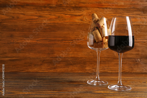 Glasses of red wine and corks on wooden background