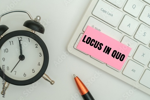 Foto A pink sticky note with LOCUS IN QUO text on a white keyboard next to an alarm clock