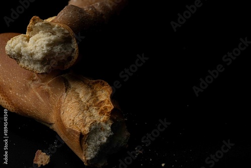 Broken fresh baguette with crumbs on a black background