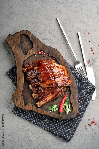 Sticky BBQ pork ribs glazed with sweet and spicy sauce on wooden serving board. Tender grilled spare ribs with rosemary and chili pepper garnish, delicious comfort food meal, top view