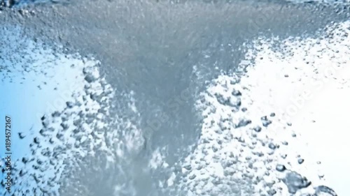 A dynamic close-up shows water vigorously swirling and bubbling A central stream of turbulent water descends amidst numerous scattered air bubbles set against a light blue background