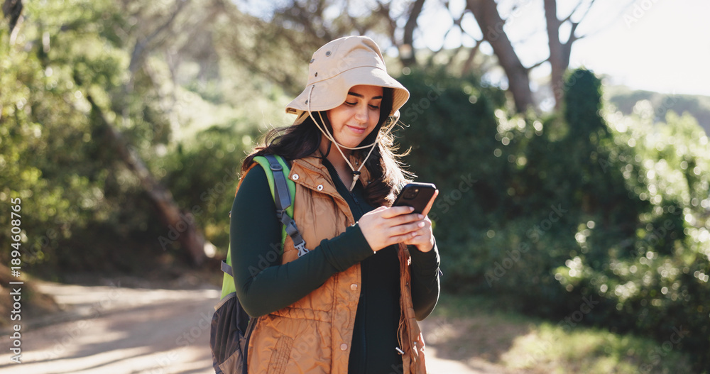 Obraz premium Hiking, chat or woman in nature with phone, message alert or location share in summer hobby. Trekking, typing or female person on path with tech, notification check or journey update on social media.