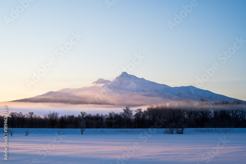 Mount Shari at sunrise in winter, Hokkaido, glowing softly above misty snowfields, capturing a serene and majestic Japanese landscape