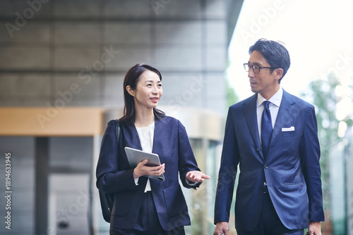 会話をしながら屋外を歩くビジネスマンとビジネスウーマン