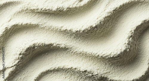 Abstract close up high angle view of creamy light yellow powder texture exhibiting soft undulating waves created by gentle sweeping motions across the surface.