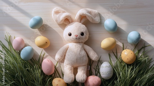 A soft beige bunny surrounded by colorful eggs and green grass. The setup includes a fluffy rabbit, green grass, and various pastel Easter eggs on wood.