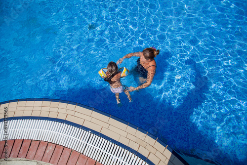 Overhead view of a mother and children swimming in a large blue resort pool.