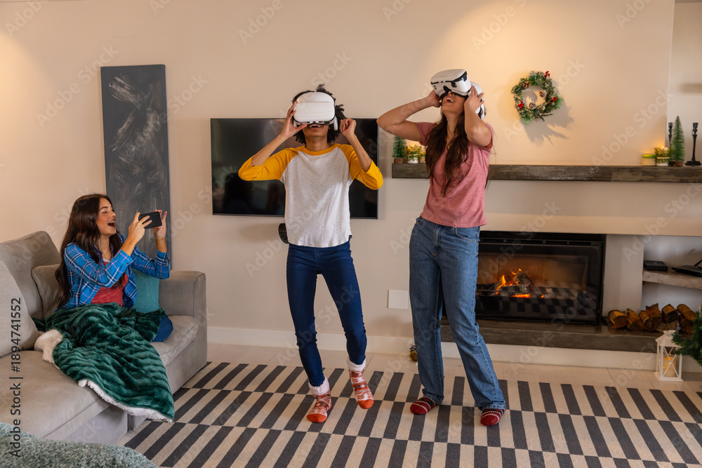 Obraz premium Diverse female friends adjusting vr headsets and recording on smartphone from couch in living room