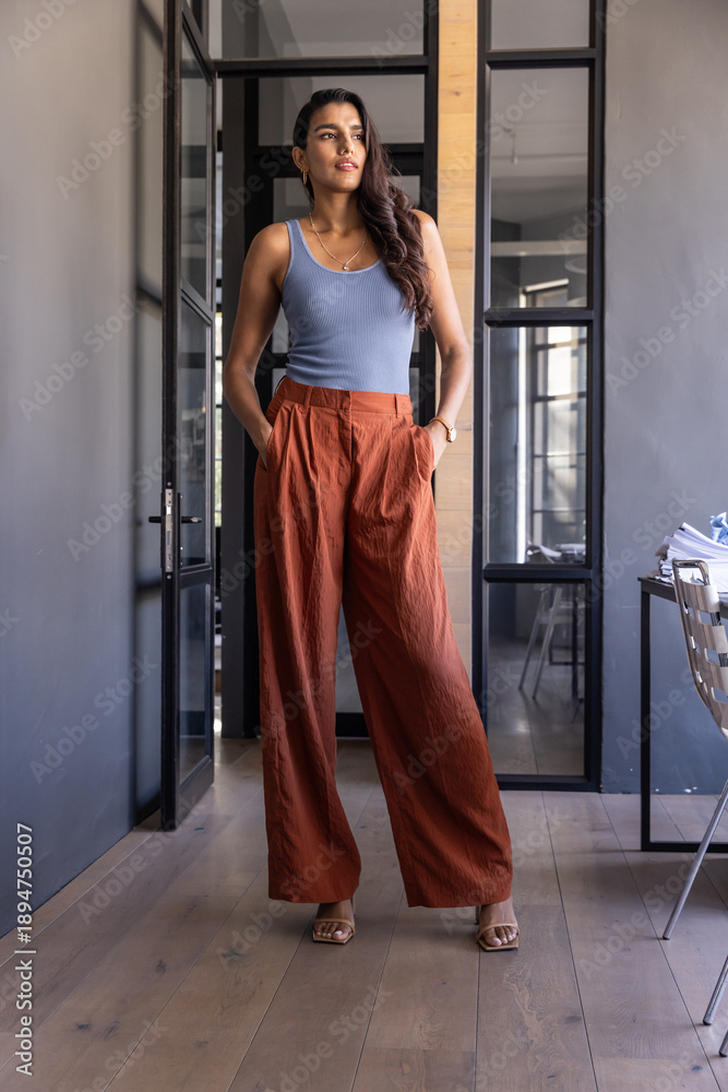 Fototapeta premium Asian indian woman standing in office doorway by black metal glass door, desk with papers