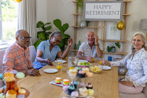 Diverse senior friends celebrating retirement in dining room at table with banner, balloons