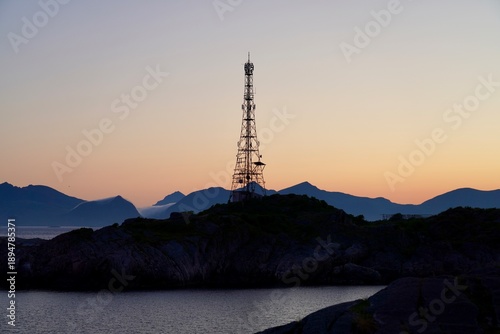 Foto A communications mast is silouetted against a pink and orange sky lit by the setting sun, in the fishing village of Henningsvaer, Norway