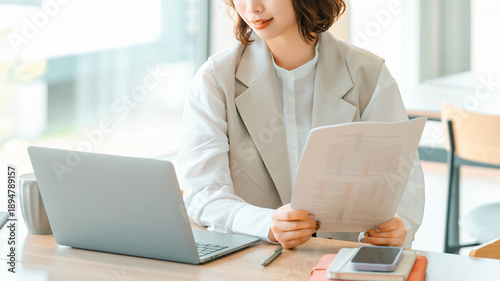 ノートパソコンで資料を確認するビジネスウーマン, Businesswoman Checking Documents on Laptop at Desk