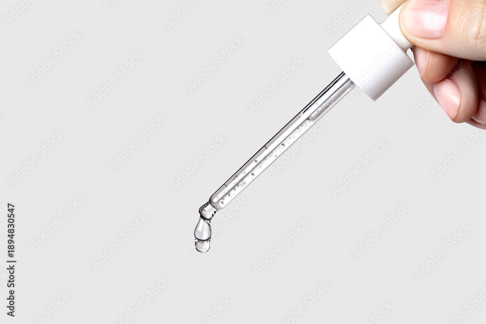 Fototapeta premium Pipette with serum in hand. Drips drop isolated on gray background, copy space photo close up