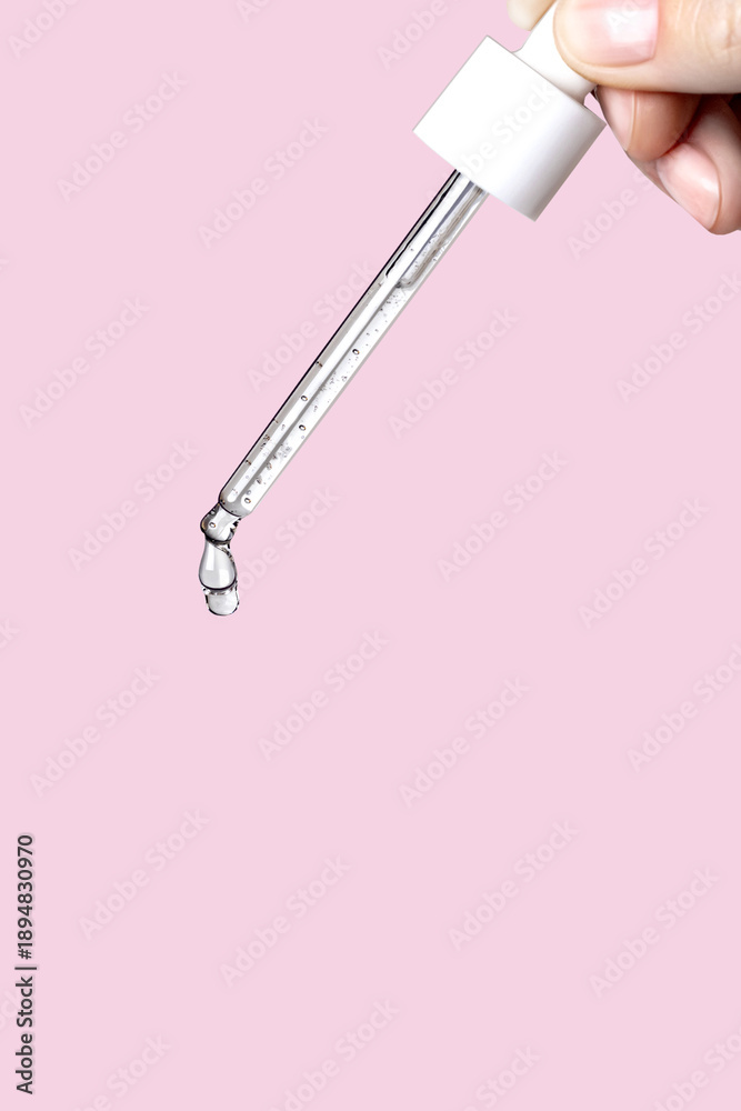 Fototapeta premium Pipette with serum in hand. Drips drop isolated on pink background, vertical photo copy space close up