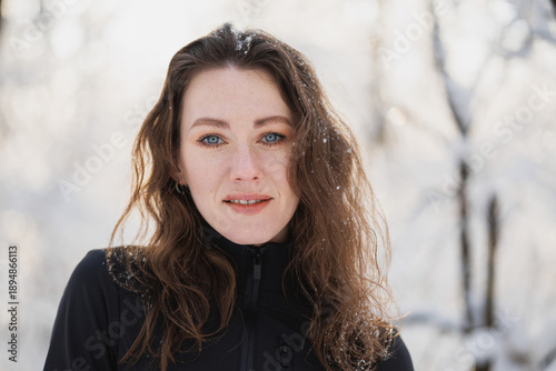 Brunette woman in active wear looking at camera in winter forest 