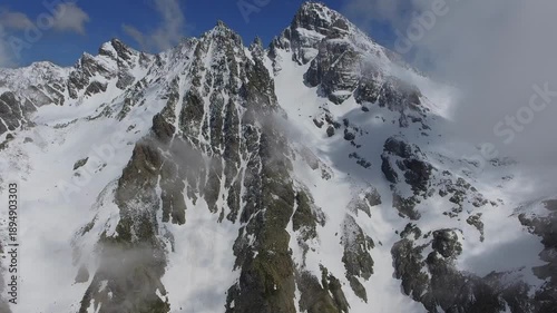 Aerial view of icy alpine lake surrounded by snowy high altitude Alps mountains peaks. Frozen water and dramatic ridges form a pristine winter landscape across Europe.